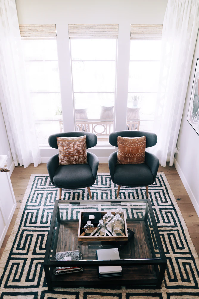 living room with a white and black carpet glass coffee table and two chairs with pillows