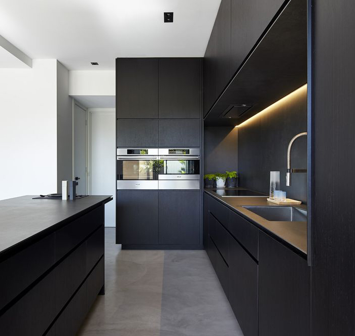 A spacious and modern black and grey kitchen with dual ovens, warm lighting and a sink